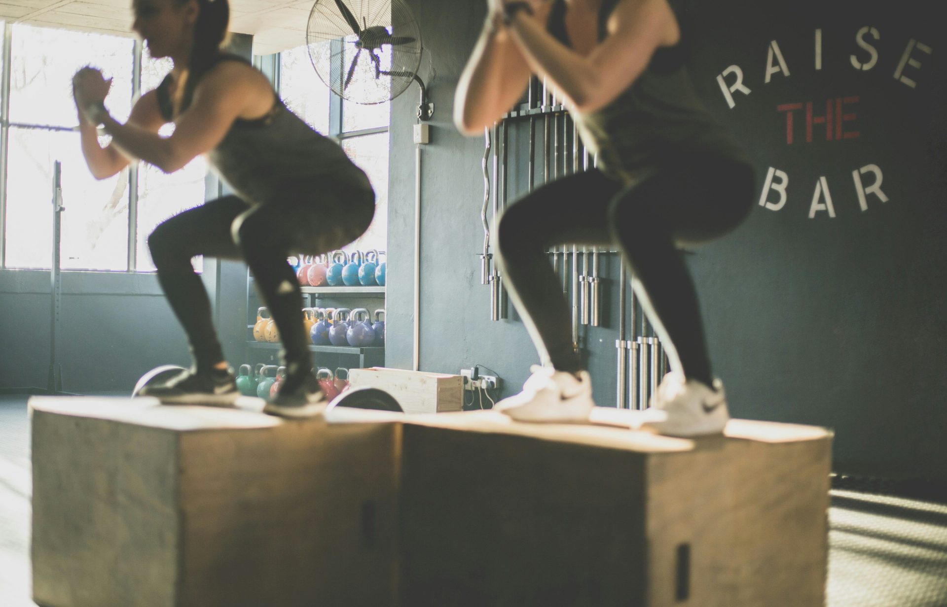 Two people performing box jumps on wooden crates in a gym